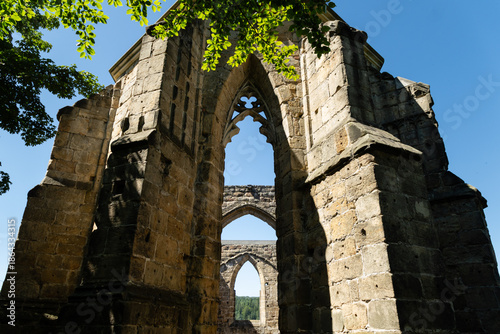 Fotografie Gothic arches towering amid green trees and blue sky in Oybin Monastery ruins on