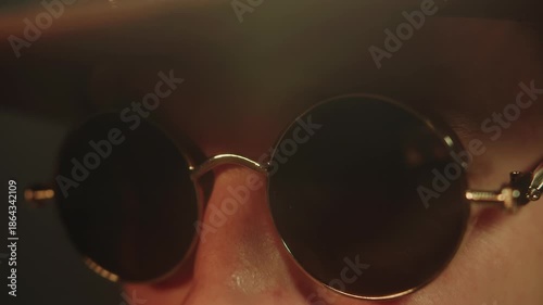 A side view of a male face wearing fashionable steampunk black sunglasses and a brown cowboy hat. A portrait studio shot of an adult stylish caucasian man who is giving a speech.