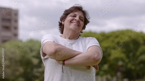 Portrait of a confident smiling middle-aged woman with arms crossed standing in a lush green park.