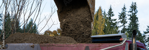 Cuadro en lienzo Excavator bucket attachment spilling dirt into a dump truck to haul away, public