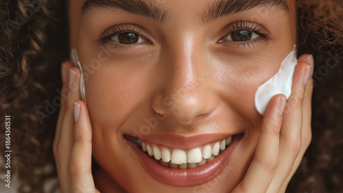Smiling woman applying face cream with hands on cheeks. Skincare self care concept.