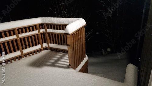 Snow covers wooden deck at night showing quiet winter scene with trees in background and fresh snowfall on ground