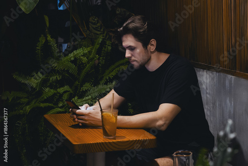 Adult caucasian male at cozy cafe with smartphone and iced drink in relaxed setting
