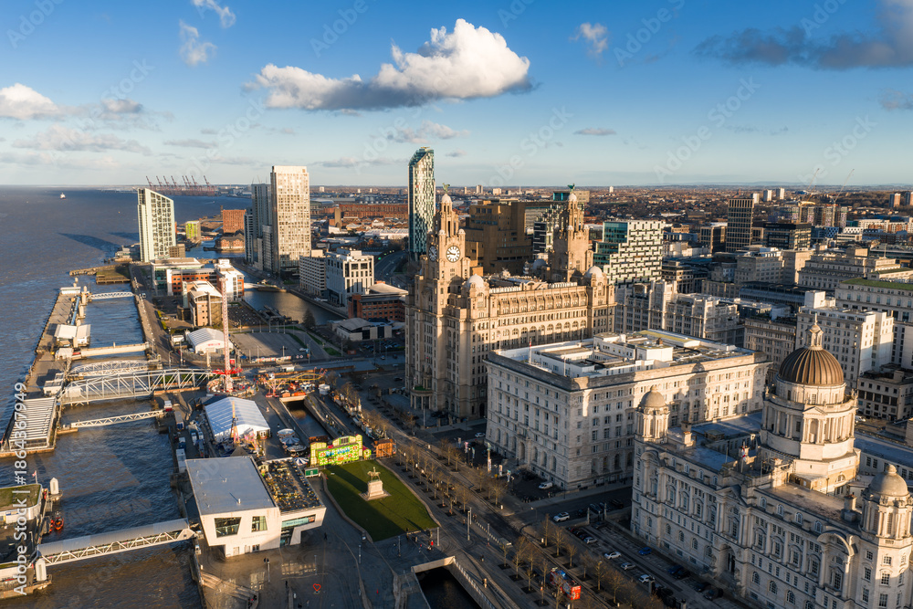 Fototapeta premium Aerial sunrise shows Liverpool waterfront, the Three Graces at Pier Head, River Mersey at left, modern towers, Museum of Liverpool, docks and promenades in warm light.