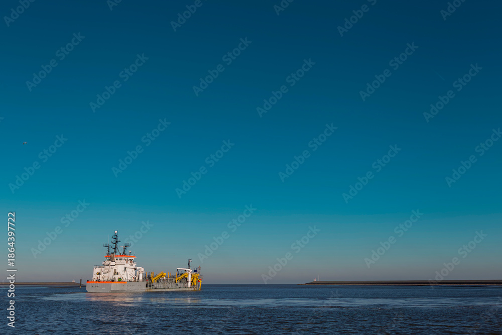 Fototapeta premium White and yellow dredging vessel working at sea under clear blue sky