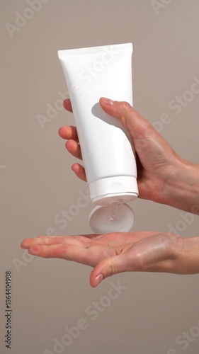 Vertical video of female hands opening white mockup tube and applying gel cream to palm of their hand on beige background. Concept of hydrating cream for freshness, rejuvenation, and beauty ritual
