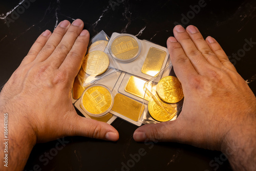 Hands protecting real gold coins and bars on dark surface symbolizing savings and investment concept