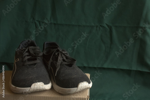 Pair of Black Athletic Sneakers on Cardboard Box with Green Fabric Background for E-commerce Retai