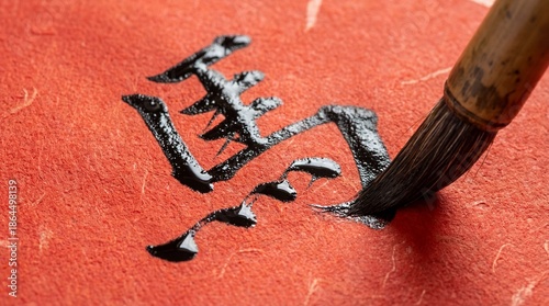 Traditional Chinese calligraphy brush writing glossy black ink characters on textured red Xuan paper. Close-up of artistic creation for Lunar New Year and spring festival.