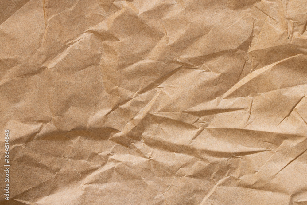 Fototapeta premium Crumpled brown kraft paper texture background, wrinkled recycled paper sheet,Top view of brown crumpled kraft paper texture background. A high-resolution close-up of wrinkled recycled paper sheet.