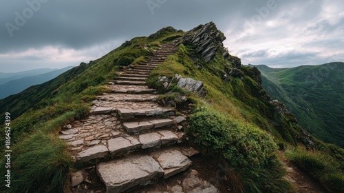A stone pathway ascends a grassy ridge towards a rocky peak under a cloudy sky, hinting at challenging terrain