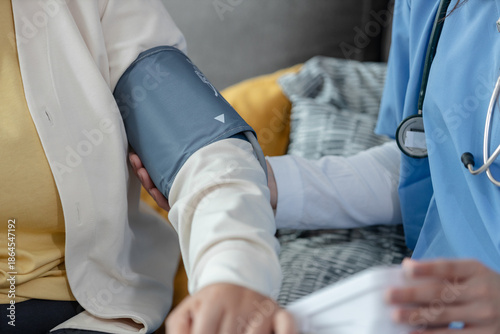 Photos Close-up of healthcare worker checking blood pressure of elderly patient at home