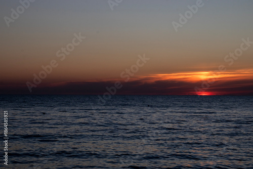 The reflection of the setting sun on the waves. A view of the sea at sunset. The sky over the sea at sunset. In the distance, bright sunbeams and reflections of the warm light of the setting sun glist