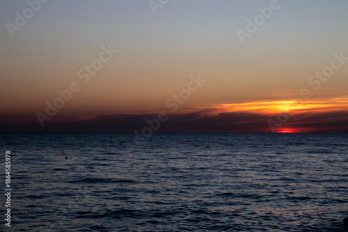 The reflection of the setting sun on the waves. A view of the sea at sunset. The sky over the sea at sunset. In the distance, bright sunbeams and reflections of the warm light of the setting sun glist