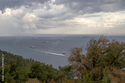 A horizontal seascape from a hillside.Moody Seascape Before a Storm with Calm Sea and Ship Silhouette on the Horizon Under an Overcast Sky
