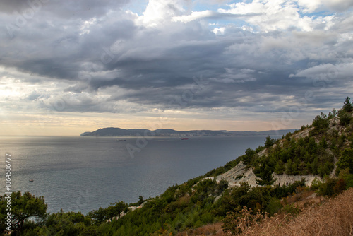 A horizontal seascape from a hillside.Moody Seascape Before a Storm with Calm Sea and Ship Silhouette on the Horizon Under an Overcast Sky