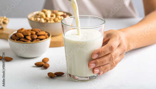Wallpaper Mural A hand pours creamy plant based milk into a glass with bowls of almonds and nuts suggesting a healthy natural beverage option Torontodigital.ca