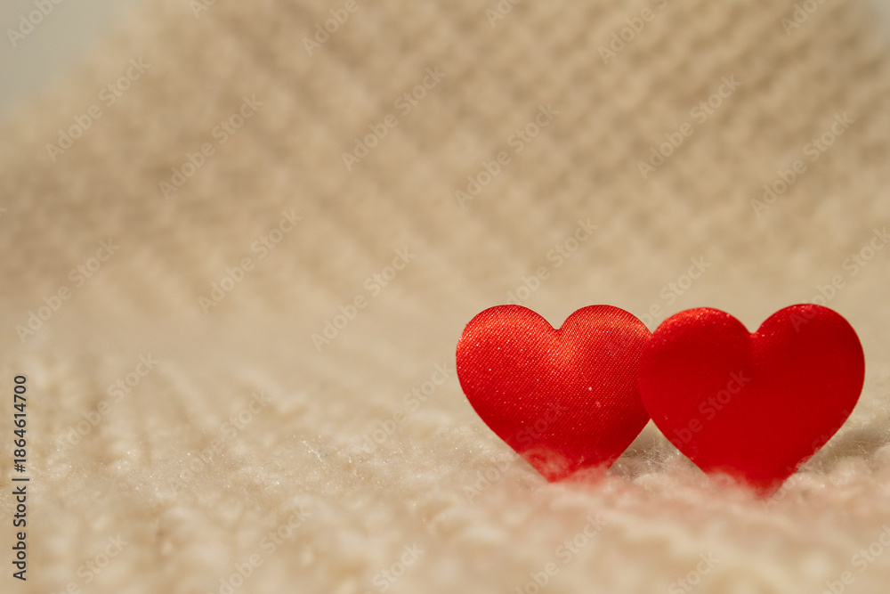 Fototapeta premium A close-up presents two red heart shapes. They sit side by side on a soft, fluffy, white blanket creating a simple Valentine's Day scene. Warm, gentle light fills the frame.