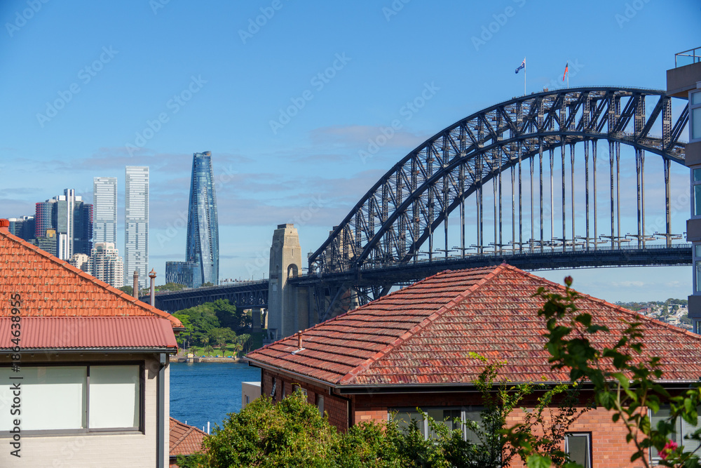 Fototapeta premium Sydney Harbour Bridge connecting city skyline and residential areas, showcasing a blend of architecture and natural beauty on a clear day.