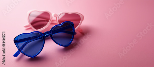 heart-shaped sunglasses in vibrant blue and soft pink tones, placed on a smooth solid pink background. 