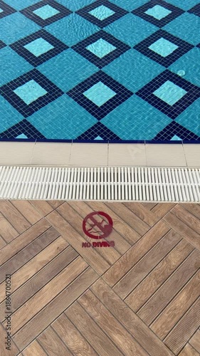 Hotel pool adorned with intricate blue mosaic tile patterns sparkles under sunlight.  Luxurious resort ambiance invites refreshing swims in stylish aquatic haven.