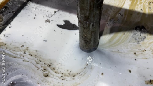 Cleaning milling machine with vacuum sucking dirty coolant fluid from the chip tray, removing metal shavings, grime, and oily residue for maintenance.