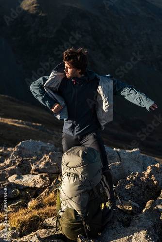 Hiker donning technical jacket for sustained mountain effort