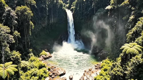 Cinematic aerial view of a powerful waterfall cascading into a turquoise pool in a dense tropical rainforest