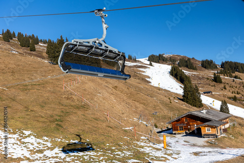 Austrian Alps ski resort shows strong contrast between white piste and snowless grass slope under blue sky. Climate warming, snow scarcity, chairlift infrastructure highlight winter tourism crisis