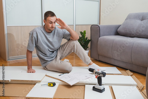 A confused man gesturing while reading furniture instructions among scattered parts and tools in a bright modern room DIY troubleshooting content hardware store advertising home renovation blogs