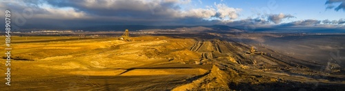 High resolution panoramic view of an open pit coal mine with mining machines, layered terrain. Industrial landscape showing large scale extraction, energy production, and environmental impact.