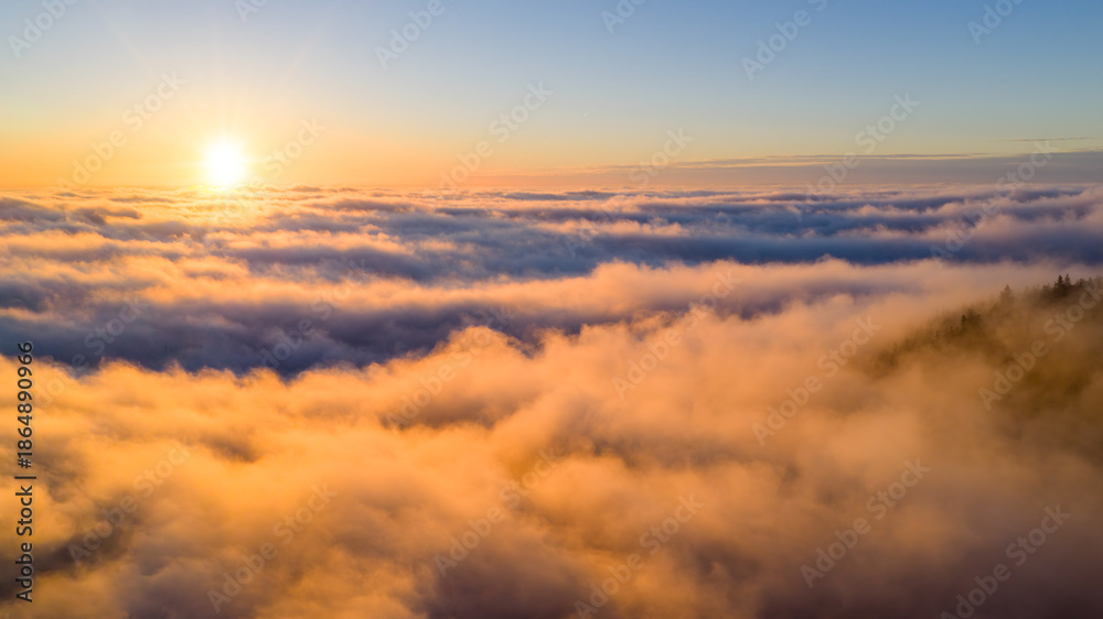 Obraz premium Golden sunrise above a sea of clouds, creating a calm and dreamy atmosphere. Warm morning light illuminates soft cloud layers, evoking freedom, serenity, and a sense of endless space.