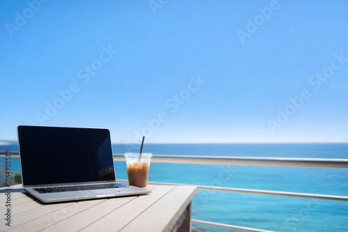 Laptop and iced coffee on balcony table with ocean view