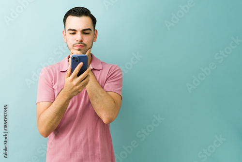 Photos Man feeling undecided and confused while holding smartphone, choosing a new app