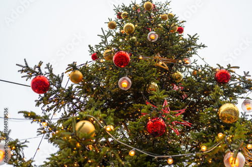 Close up detail of christmas tree decorations with red and gold baubles, star shaped ornaments and warm lights imitating fire, festive holiday atmosphere in brno city