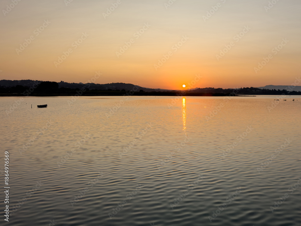Obraz premium Warm golden sunset over Chalkiopoulos Lagoon near Corfu Airport, Greece. Calm water reflecting the sun, summer evening