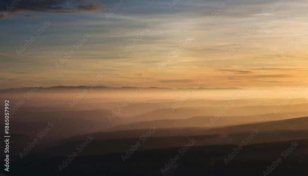 Fototapeta premium Sunset over layered mountain ranges with mist and a colorful sky.