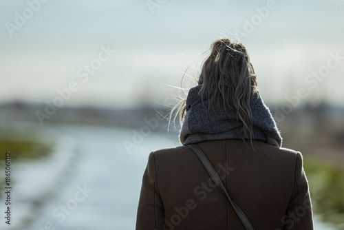 Woman in brown coat walking alone on rural road with blurred background