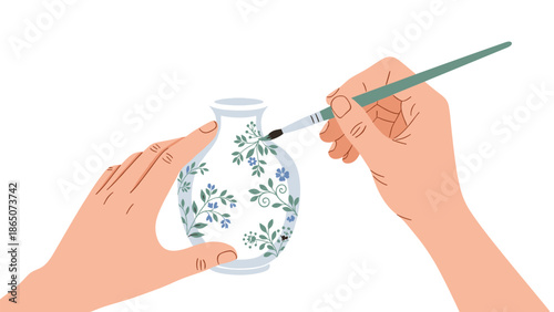 Close-up view of hands delicately painting intricate blue and green floral patterns onto a white ceramic vase, showcasing a creative hobby and the art of pottery decoration.