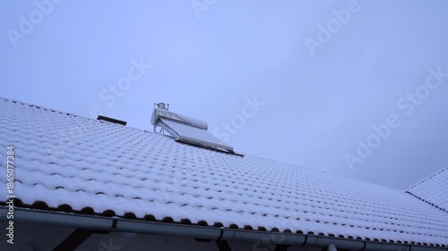Durable stainless steel solar water heater boiler on rooftop at wintertime, slow pan shot.