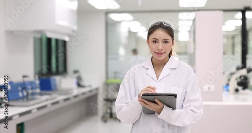 Female scientist wearing a lab coat holding a tablet and smiling to camera in a modern laboratory	
