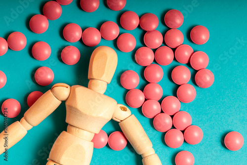 A wooden figure is laying on a pile of pink pills