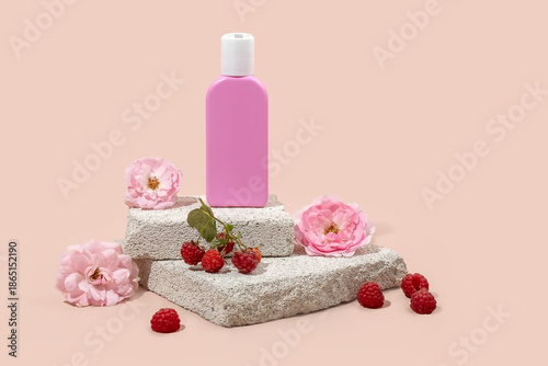 bottle for skin care cosmetics on a stone podium , raspberry berries and rose flowers on a beige background