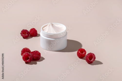 a jar of face or hand cream and fresh raspberries on a pink background