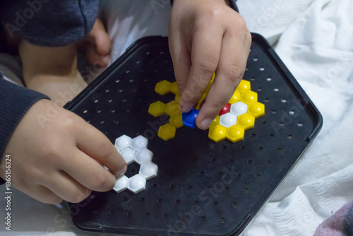 Close-up of child's hands playing with hexagonal mosaic puzzle on a black board.