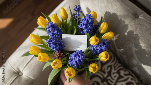 Vibrant Yellow Tulips and Blue Hyacinths Bouquet with Blank Card Held by Hand on Sofa Cushion