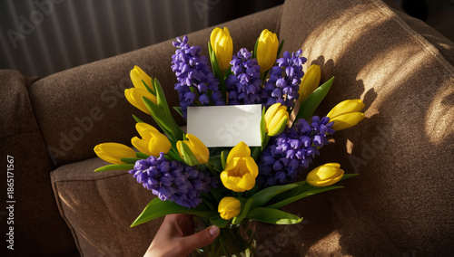 Vibrant Yellow Tulips and Purple Flowers Bouquet with Blank Card on Brown Sofa under Soft Natural Light