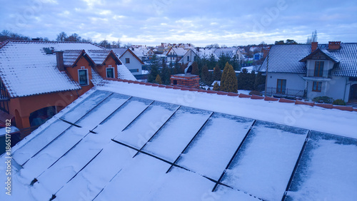 Aerial view of solar panels on the roof of a house covered with snow on a frozen winter day.