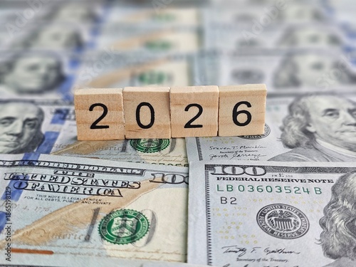 Banknotes and wooden blocks showing the year 2026 on a table with more money in the background concept