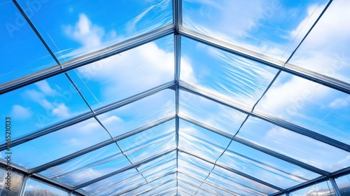 View upwards through the transparent roof of a large outdoor event tent with a clear blue sky and white clouds visible above the metal framework